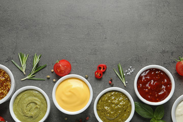 Bowls with different sauces and ingredients on gray background, flat lay. Space for text