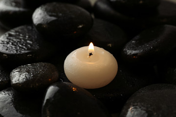 Small burning candle on beautiful wet spa stones