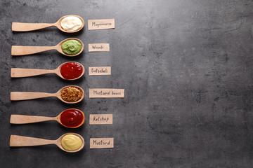 Different sauces in spoons and name tags on gray background, flat lay. Space for text