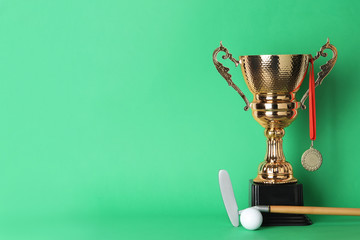 Golden trophy cup, medal, golf club and ball on color background. Space for text