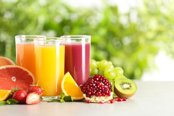 Three glasses with different juices and fresh fruits on table against blurred background. Space for text