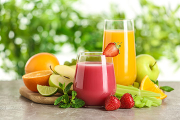 Glasses with different juices and fresh fruits on table against blurred background