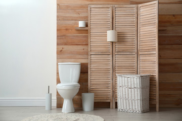 Toilet bowl near wooden wall in modern bathroom interior