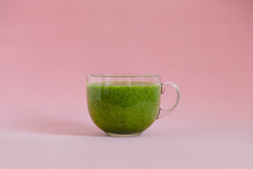 Healthy green smoothie in a glass cup on pink background