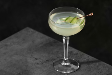 Glass of martini with cucumber on grey table against dark background. Space for text