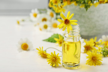 Fototapeta na wymiar Bottle of essential oil with yellow flowers on table. Space for text