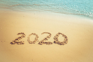Happy New Year 2020 concept, 2020 number lettering on the sea beach, wave and golden light of sunset.