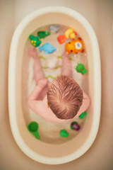 Cute little girl playing with rubber toys in small bathtub