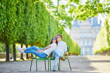 Happy romantic couple in Paris, sitting on traditional green metal chairs in Tuileries garden