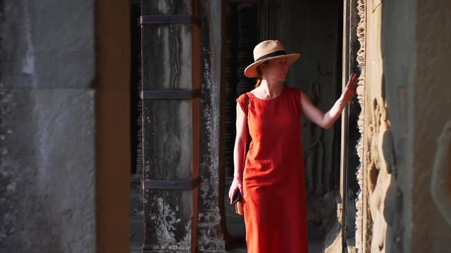 Woman in red dress is exploring corridors and amazing carvingsg of ancient Angkor Wat temple, built in 12th century in Cambodia and dedicated to Vishnu. Cambodia