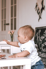 Fototapeta premium Happy baby boy small playing with toys in kids room in jeans and white t-shirt