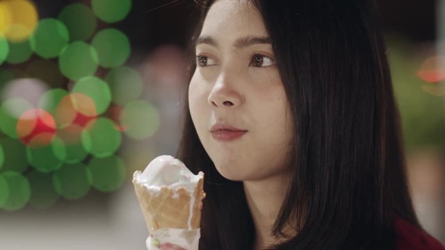 Asian young woman travel in Bangkok, Thailand, beautiful female feeling happy walking and eating ice cream at The Khao San Road. Women travel eat street food in Thailand concept. Slow motion shot.