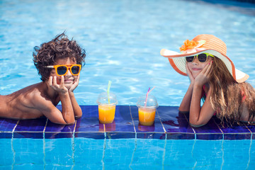 Two kids girl and boy drink juice in the pool and have fun. Children and summer concept
