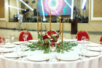 Festively decorated round banquet table in the restaurant. Fresh flowers are golden candles and red chairs. expensively rich