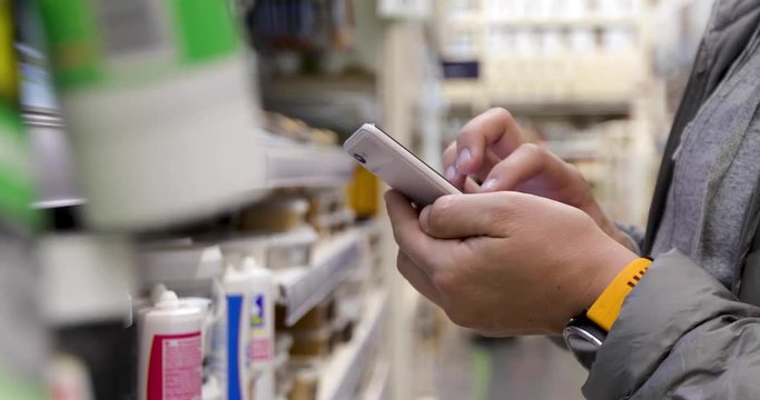 Crop man in checks the goods in the application in the smartphone in the hardware store close up