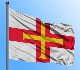 Guernsey flag waving in the deep blue sky background. Isolated national flag. Macro view shot.
