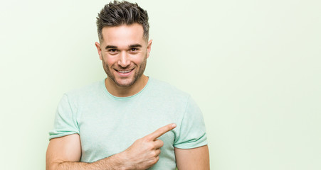 Young handsome man against a green background smiling and pointing aside, showing something at blank space.