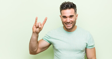 Young handsome man against a green background showing a horns gesture as a revolution concept.