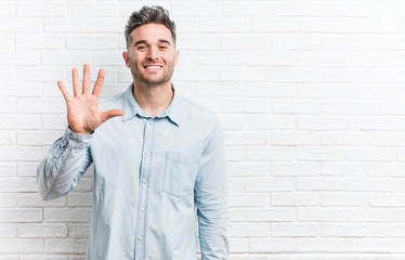 Young handsome man against a bricks wall smiling cheerful showing number five with fingers.