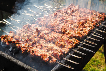 Cooking of tasty meat on skewers - pork shashlick outdoors on a grill, with smoke, closeup