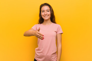 Fototapeta premium Young european woman isolated over yellow background stretching hand at camera in greeting gesture.
