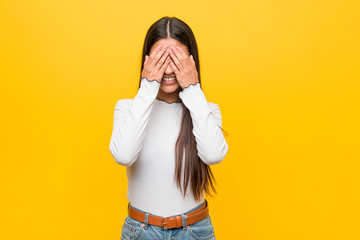 Young pretty arab woman against a yellow background covers eyes with hands, smiles broadly waiting for a surprise.