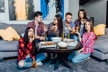 Group of young multi-ethnic friends with pizza and bottles of drink celebrating in home interior..