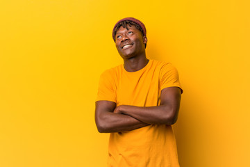 Young black man wearing rastas over yellow background smiling confident with crossed arms.