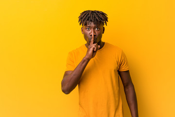 Young black man wearing rastas over yellow background keeping a secret or asking for silence.