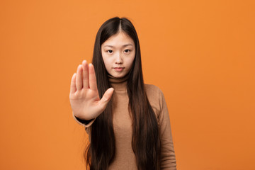 Young pretty chinese woman standing with outstretched hand showing stop sign, preventing you.