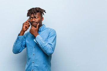 Young rasta black man holding a phone looking sideways with doubtful and skeptical expression.