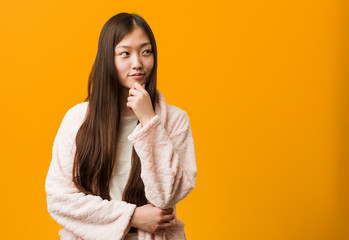 Young chinese woman in pajama looking sideways with doubtful and skeptical expression.