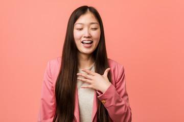 Young business chinese woman wearing pink suit laughs out loudly keeping hand on chest.