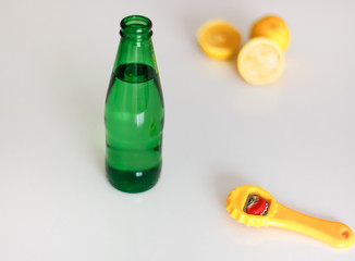 Green glass bottle of fizzy drink and bottle opener on the white background. Drinking mineral...