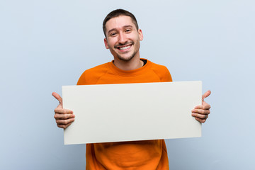 Young caucasian man holding a placard smiling and raising thumb up