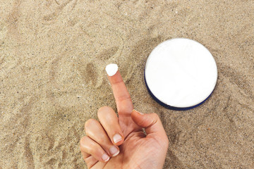 Female hand apply cosmetic cream on sand 
