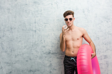Obraz premium Young man holding a pink inflatable donut wearing a swimsuit upset screaming with tense hands.
