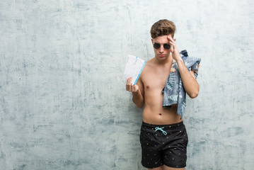 Young man wearing a swimsuit holding air tickets touching temples and having headache.