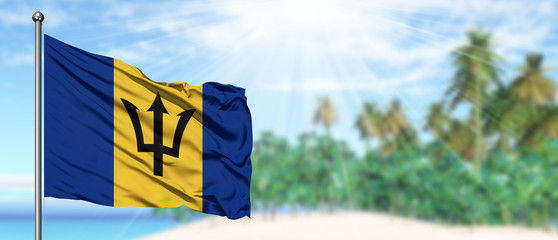 Waving Barbados flag in the sunny blue sky with summer beach background. Vacation theme, holiday...