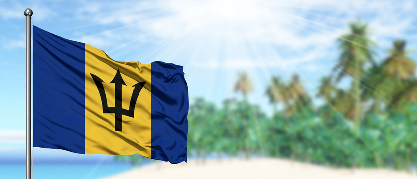 Waving Barbados flag in the sunny blue sky with summer beach background. Vacation theme, holiday concept.