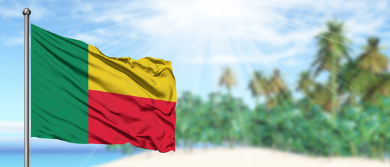 Waving Benin flag in the sunny blue sky with summer beach background. Vacation theme, holiday concept.