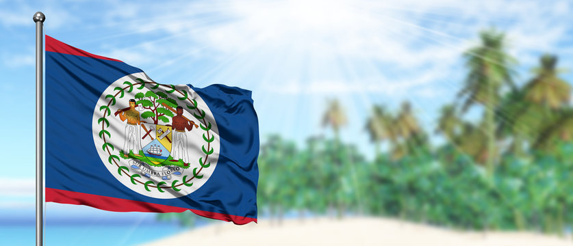Waving Belize flag in the sunny blue sky with summer beach background. Vacation theme, holiday concept.