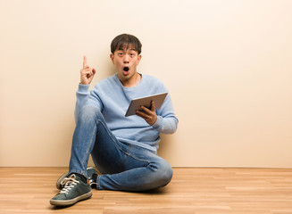 Young chinese man sitting using his tablet having a great idea, concept of creativity