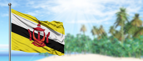 Waving Brunei flag in the sunny blue sky with summer beach background. Vacation theme, holiday concept.