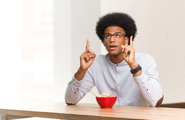 Fototapeta na wymiar Young black man having a breakfast surprised pointing up to show something