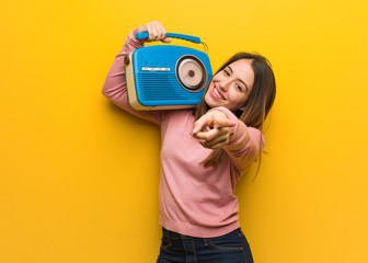 Young cute woman holding a vintage radio cheerful and smiling pointing to front