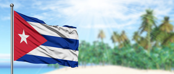 Waving Cuba flag in the sunny blue sky with summer beach background. Vacation theme, holiday concept.