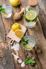 Bottle and two glasses of fresh lemonade with lemon slices, mint and ice on old wooden planks