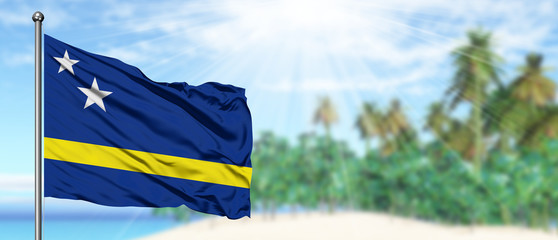 Waving Curacao flag in the sunny blue sky with summer beach background. Vacation theme, holiday concept.