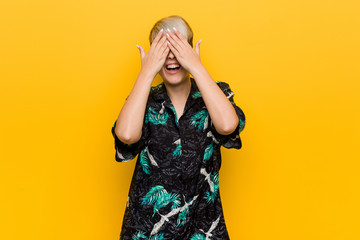 Young curvy woman wearing a summer look covers eyes with hands, smiles broadly waiting for a surprise.